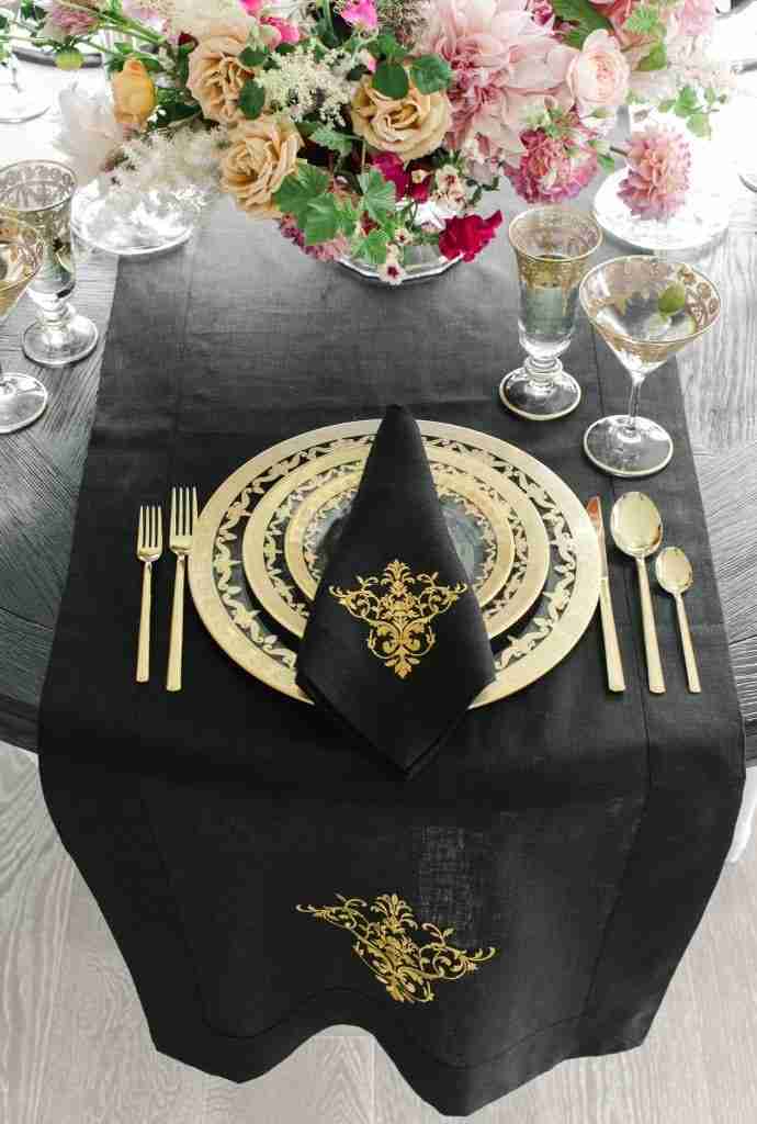Tablescape with gold plates and black linen napkins from Crown Linen