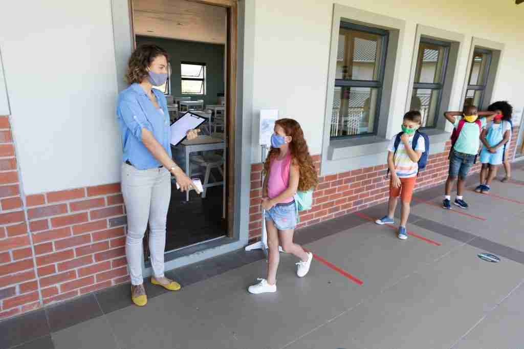 Female teacher wearing face mask pointing girl to stand on the marker