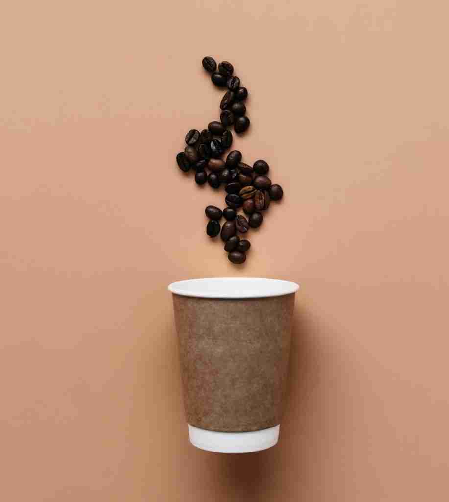 Beige background with paper coffee cup, coffee beans steam from hot coffee