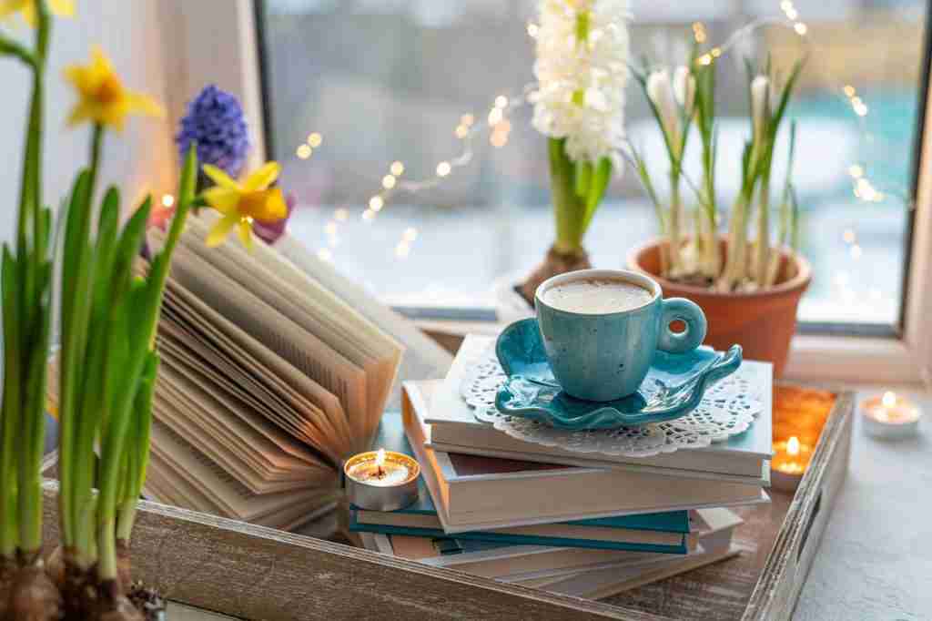 Coffee cup, open book, beautiful flowers, sparkle candles on window with bokeh. Reading and coffee