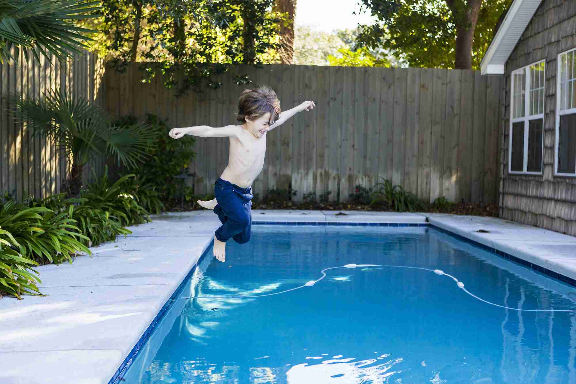 A six year old boy leaping into a swimming pool