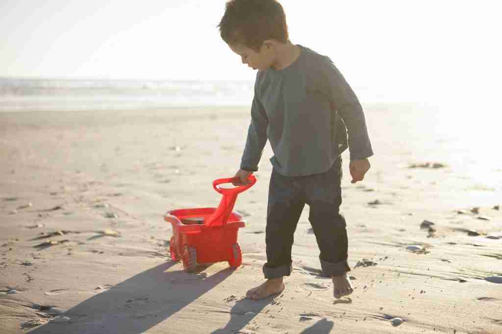 Boy pulling toy truck filled with sand along beach