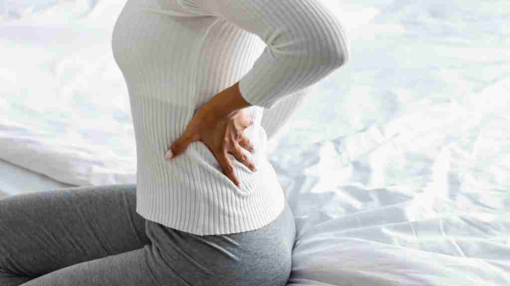 Closeup of black woman with back pain sitting on bed