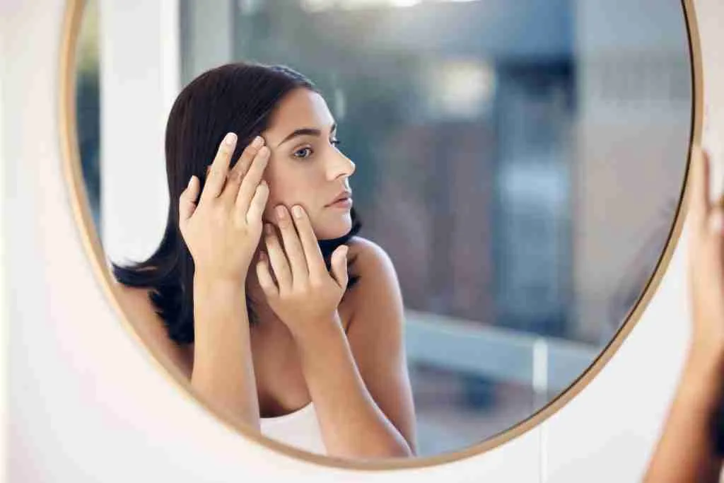 Skincare, facial and woman by a mirror to check for acne breakout or pimples while cleaning face in
