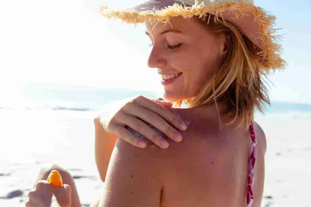 Woman applying sunscreen on her back at the beach