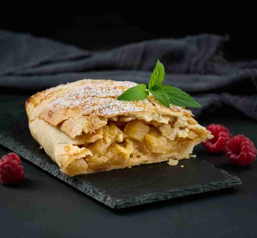 Baked strudel with apples sprinkled with powdered sugar on a black board, delicious dessert