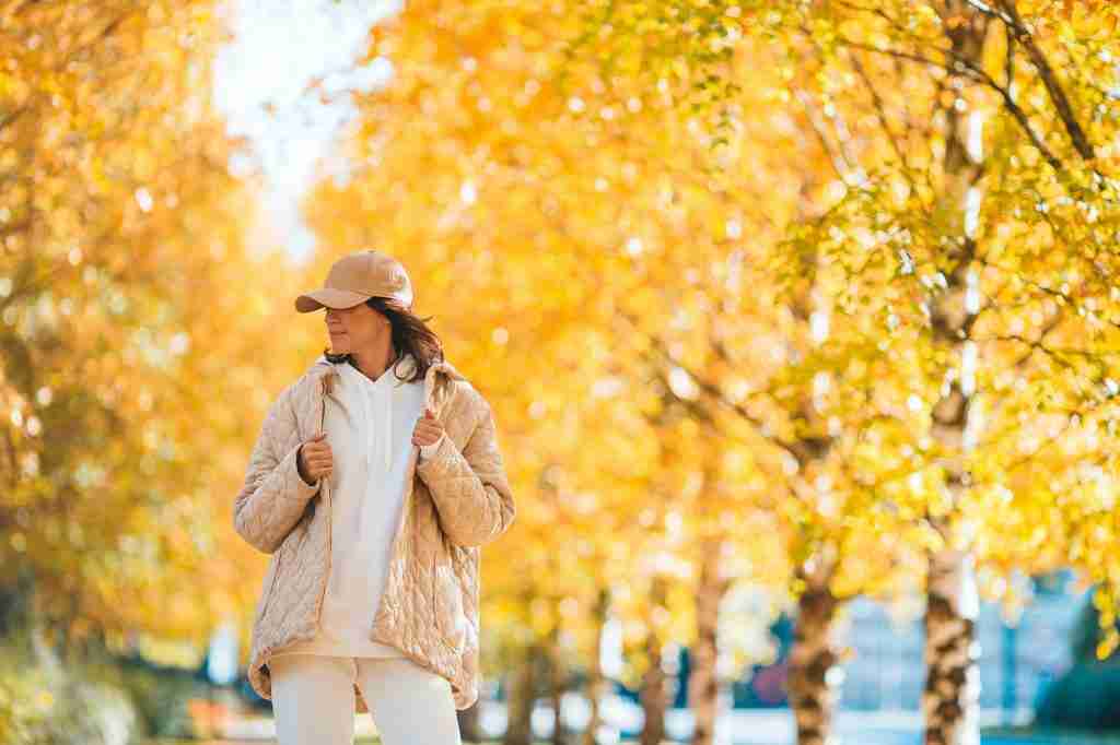 Fall concept - beautiful woman drinking coffee in autumn park under fall foliage