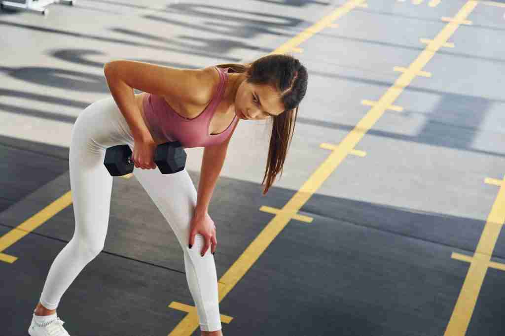 In white pants. Beautiful young woman with slim body type is in the gym