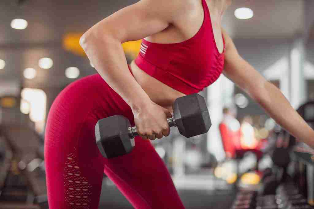 Crop adult sportswoman training with dumbbell