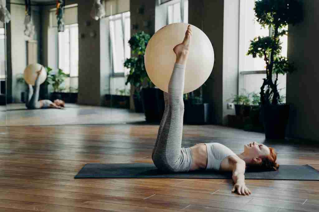 Young woman doing exercises for legs with pilates ball while lying on yoga mat