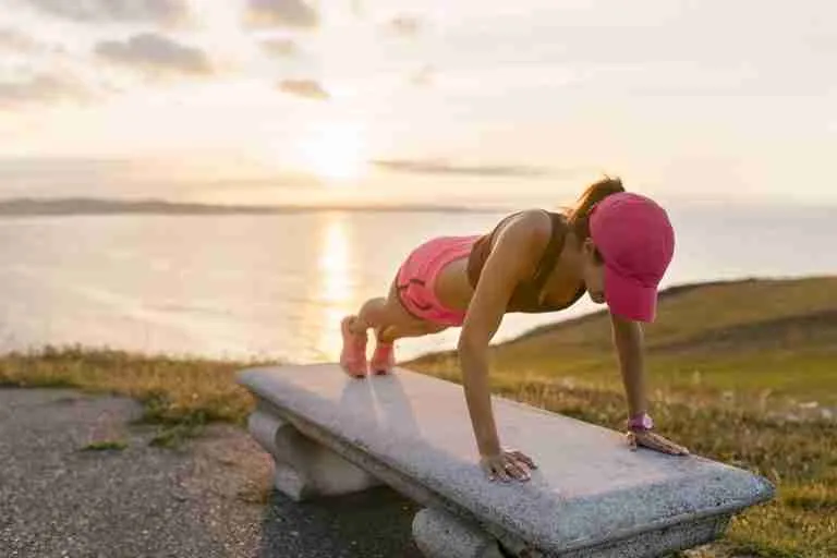 Young woman doing strength training on a bench at the sea