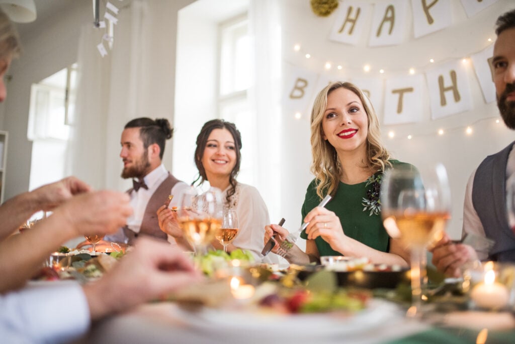 A big family sitting at a table on a indoor birthday party, eating.