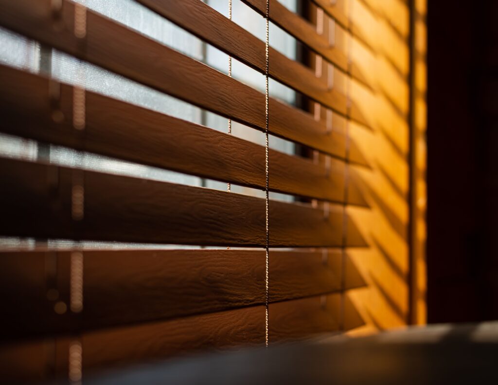 Wooden blinds next to a window with sunlight on the side