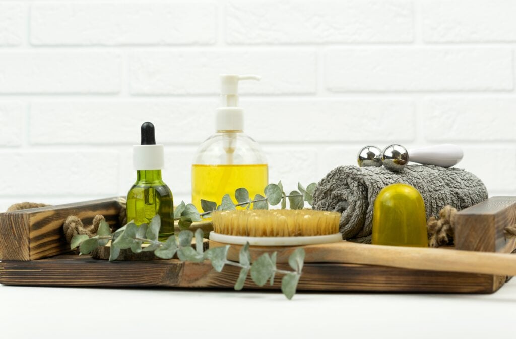 A CBD green oil, face roller, a brush for dry massage standing on a wooden tray in a bathroom