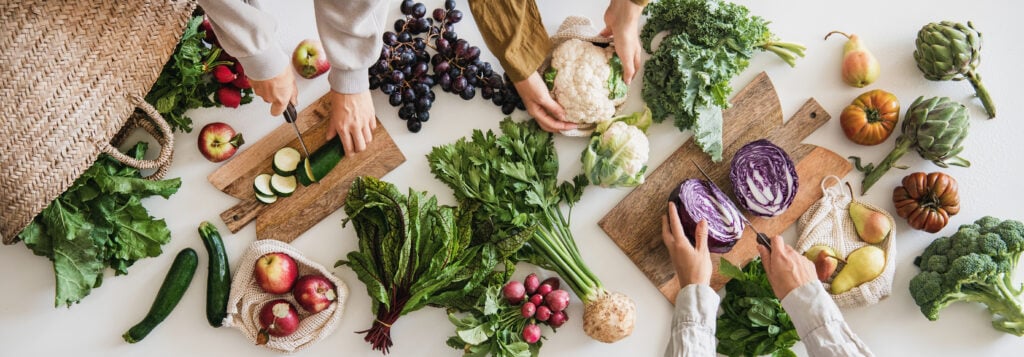 Female hands cutting various veggies and fruits, top view