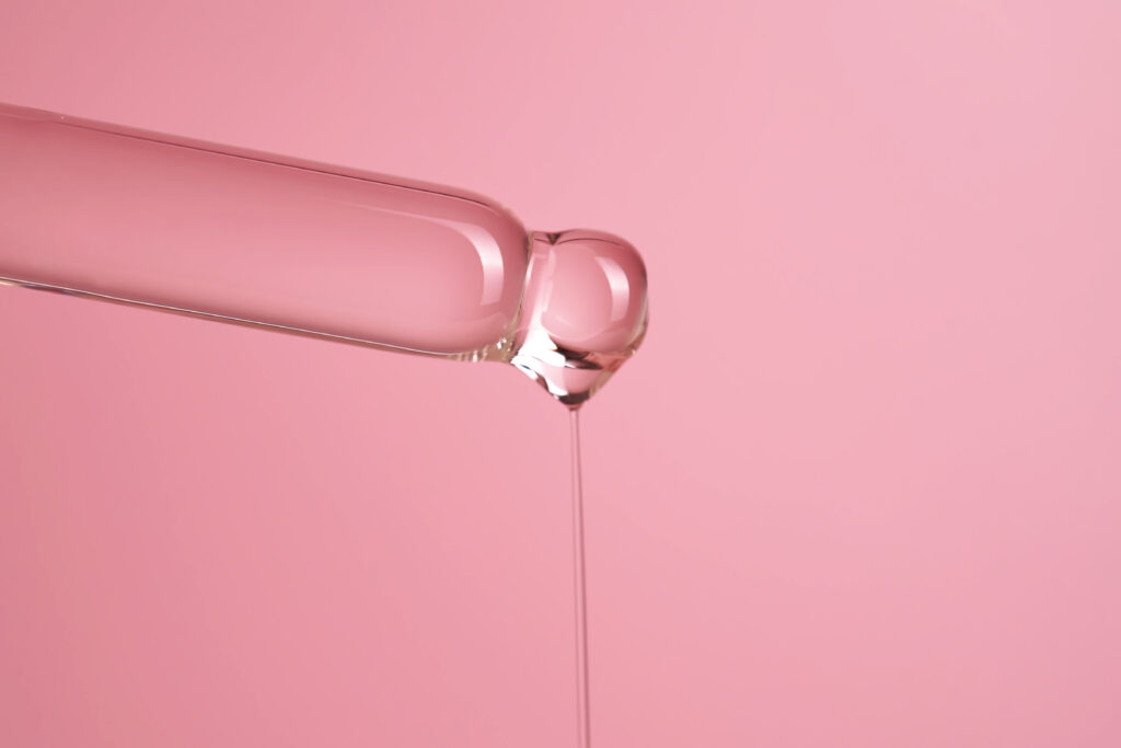 Dropper with serum or cosmetic oil on a pink background.