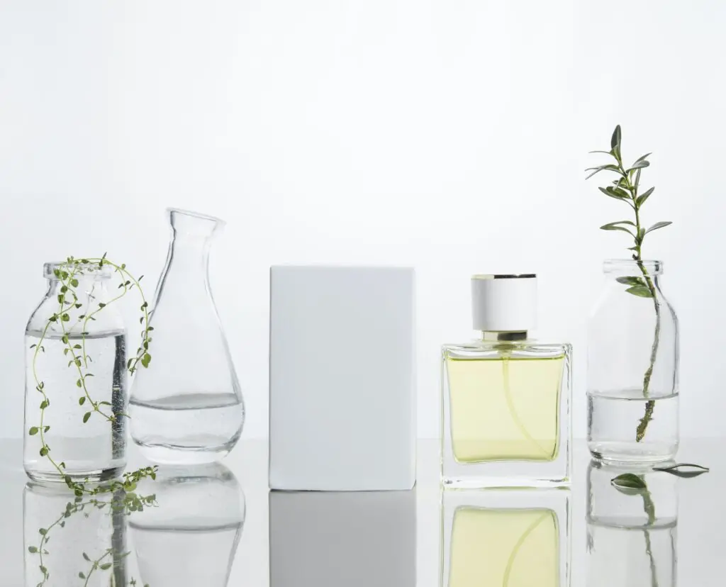 Perfume bottles and vases with fresh branches and flowers on a glass background.