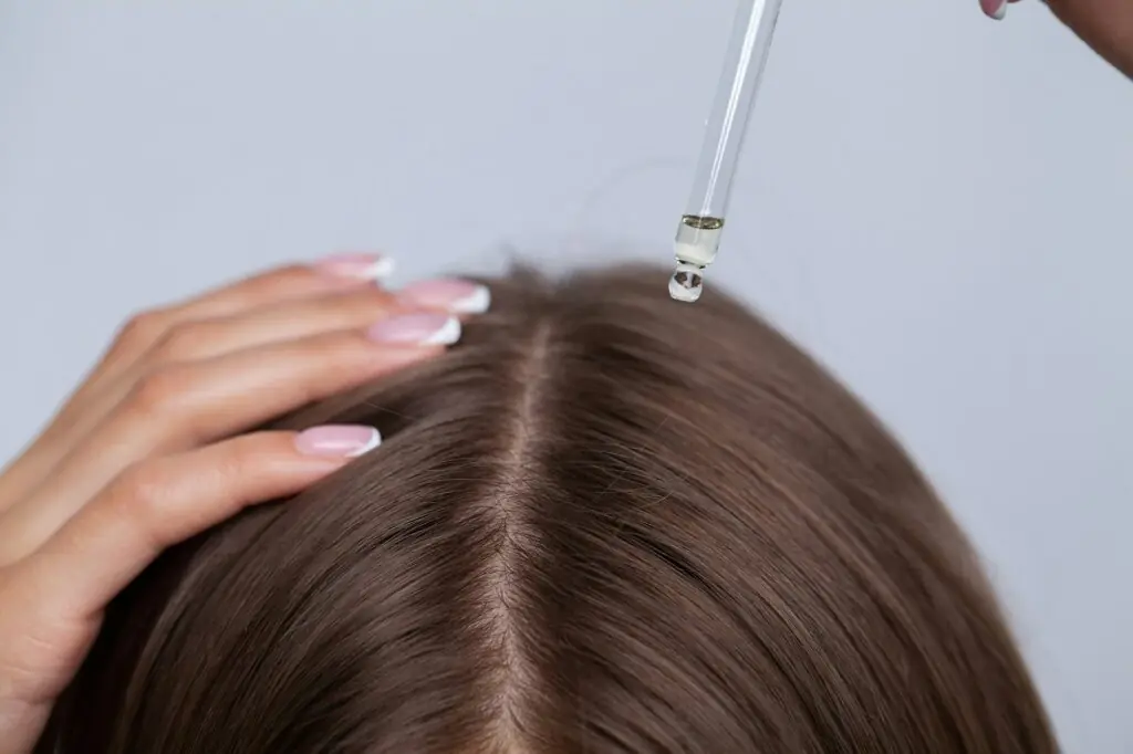 Young woman applying oil onto hair in bathroom