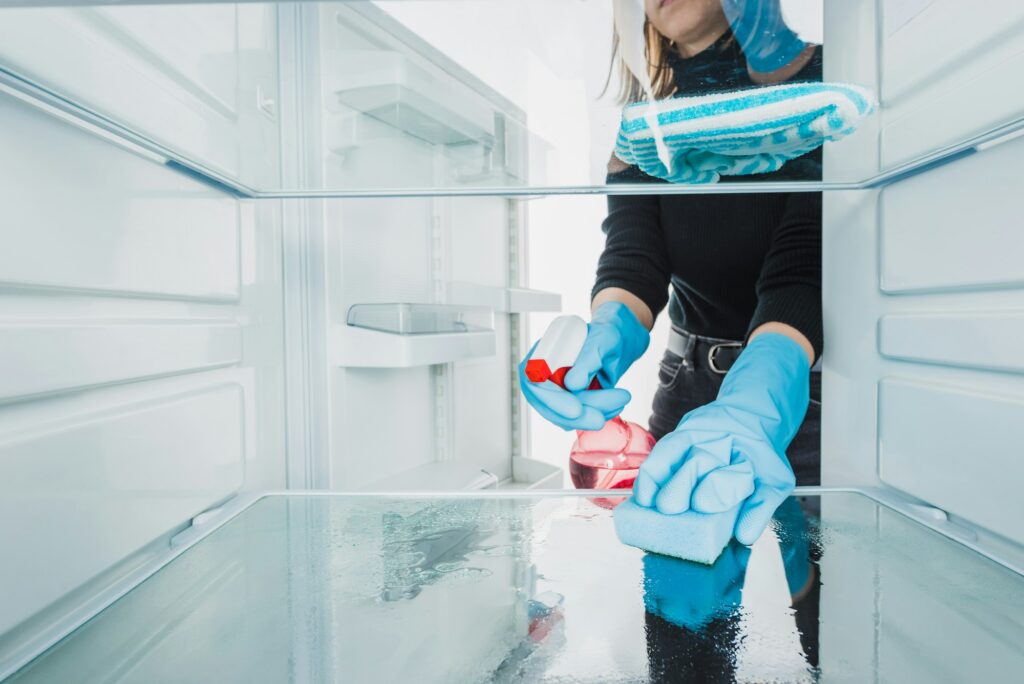 Cropped view of woman in rubber gloves cleaning refrigerator with detergent isolated on white