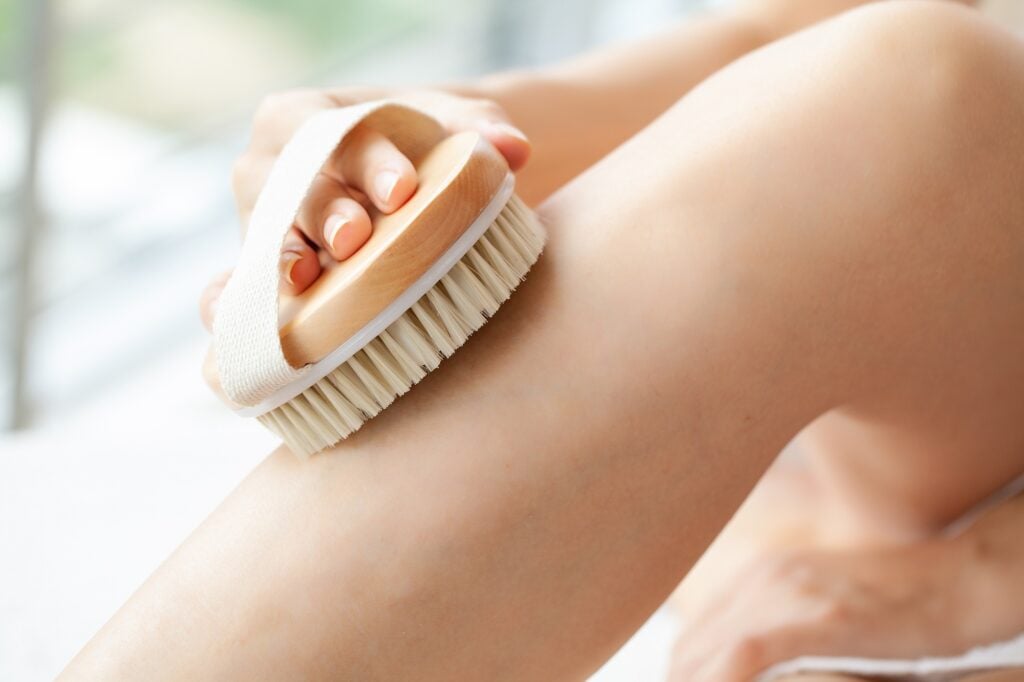 Cellulite treatment, woman arm holding dry brush to of her leg.